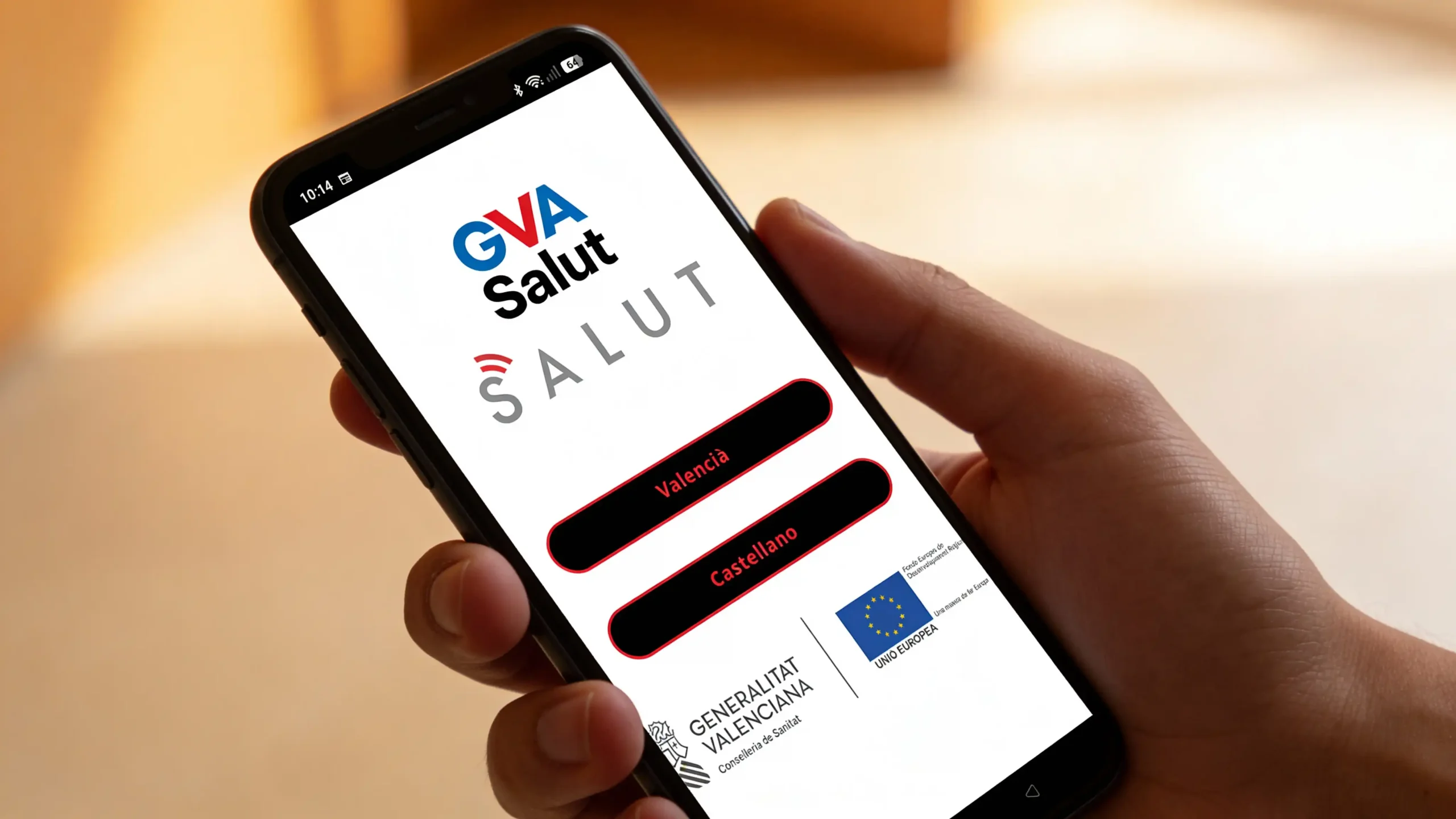 Hand hält Smartphone mit geöffnetem Startbildschirm der GVA Salut App, auf dem die Sprachoptionen „Valencià“ und „Castellano“ angezeigt werden.