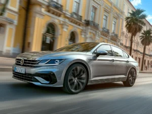 Silberner Volkswagen fährt dynamisch vor historischer Stadtfassade mit Palmen